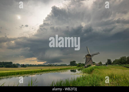 Supercell thunderstorm mit Rotierende wallcloud über die Landschaft von Holland. Klassische niederländische Szene mit einem Kanal und Windmühle. Stockfoto