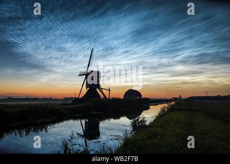 Nachtaktive Wolken (NLC), Blick nach Norden in der Mittsommernacht. Klassische holländische Szene mit Kanal- und Windmühlensilhouette gegen den Dämmerungshimmel. Stockfoto