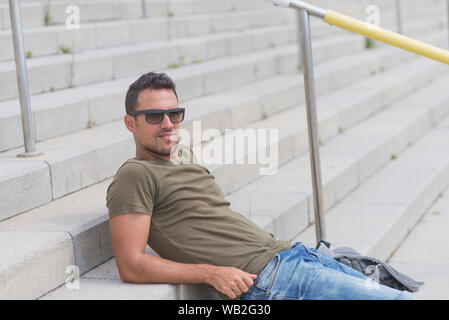Junger Mann mit Sonnenbrille auf der Treppe sitzen entspannt Stockfoto