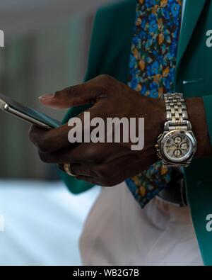 Nahaufnahme eines afrikanischen Mannes mit grünem Anzug und Eine graue Armbanduhr mit einem Smartphone Stockfoto