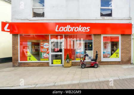 Ein Mobility Scooter außerhalb einer Ladbrokes betting Shop geparkt. Stockfoto