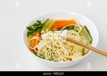 Traditionelle asiatische Suppe mit Tofu, Käse, Nudeln, Karotten und Zucchini auf weißem Hintergrund. Dieses Gericht enthält in der Regel Bouillon und Gemüse Stockfoto