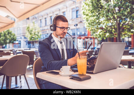 Hübscher junger Mann an Street Cafe sitzen haben business meeting via Videokonferenz auf einem Laptop Stockfoto