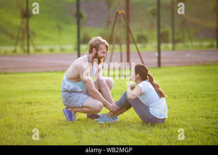 Ups fitness Paar Ausübung außerhalb im Gras sitzen Sitzen. Passen Menschen, Cross Training. Frau tun Bauch crunches drücken Sie die Übung mit Stockfoto
