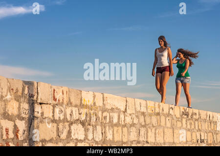 Zwei Mädchen gehen entlang der Oberseite der Wellenbrecher, Kaštel Lukšić Hafen, Kroatien Stockfoto