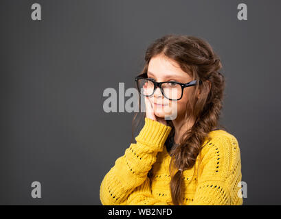 Denken Ernst kid Mädchen scratch das Gesicht in Brillen Studio auf grauem Hintergrund. Closeup Portrait mit leeren Platz kopieren Stockfoto