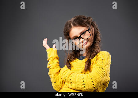 Denken Angry Kid Mädchen gestikulierend die Hand in Brillen Studio auf grauem Hintergrund. Closeup Portrait mit leeren Platz kopieren Stockfoto