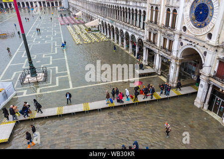 Menschen auf erhöhten Plattformen am Torbogen auf die merceria während der Acqua Alta (hohe Wasser) Fall, Markusplatz, Venedig, Italien Stockfoto