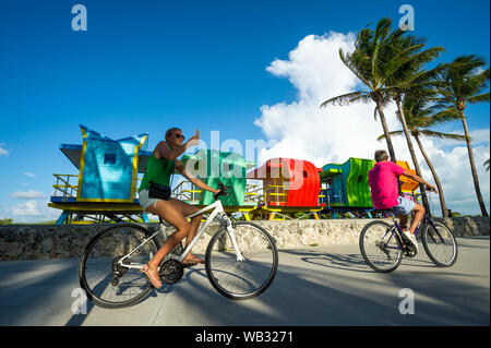 MIAMI - September 15, 2018: ein paar Fahrräder fahren vorbei an einer Reihe von bunten Rettungstürme warten auf Platzierung in South Beach. Stockfoto