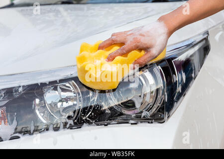 Frau hand mit gelben Schwamm waschen Scheinwerfer modernes Auto oder Reinigung Automobil. Auto waschen Konzept Stockfoto