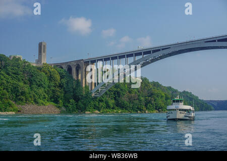 Niagara Falls, Ontario, Kanada: Die Rainbow International Bridge über den Niagara Schlucht, der Regenbogen Carillon Turm, ein Mädchen des Nebels touristische Boot. Stockfoto