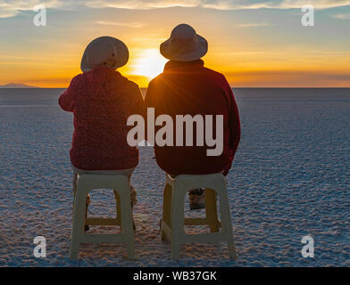 Ein paar Touristen sitzen auf Bänken und genießen Sie einen Sonnenuntergang in der Uyuni Salzsee Wüste mit Lens Flare, Anden Altiplano in Bolivien. Stockfoto