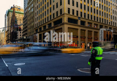 New York, USA - Dezember 07, 2018: Verschwommenes Gelbe Taxis Geschwindigkeit Vergangenheit Menschenmassen und verkehrspolizist an einer belebten Kreuzung auf der 5th Avenue, Manhattan Stockfoto