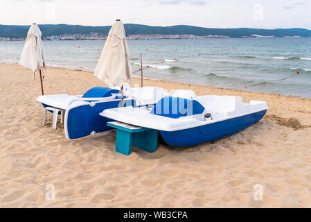 Zwei Tretboote stehen am Ufer, sowohl gefaltet Sonnenschirme in Sonnenstrand, Bulgarien. Im Hintergrund das Schwarze Meer. Stockfoto