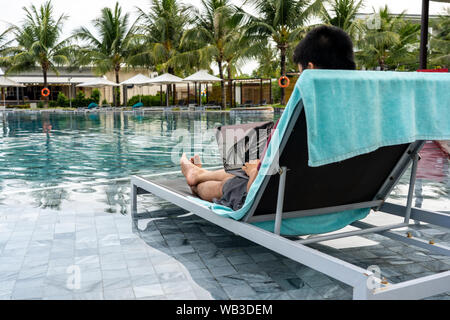 Junge Freiberufler mit Laptop am Pool im Sommer Stockfoto