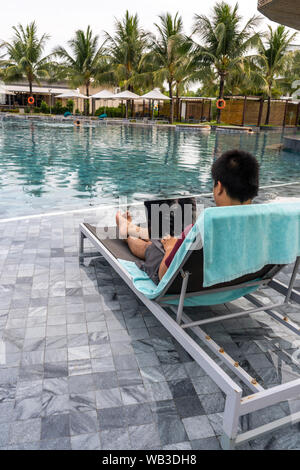 Junge Unternehmer mit Laptop am Pool im Sommerurlaub Stockfoto