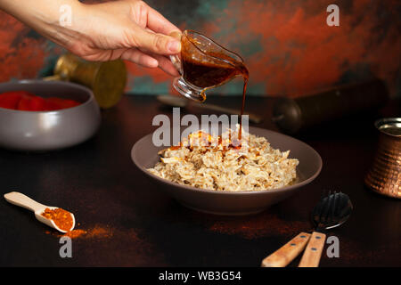 Traditionelle für türkische, griechische und iranische Küche, ein Gericht namens Keskek. Eingelegte Paprika, Butter und Paprikapulver. Die Soße auf den Teller gegossen Stockfoto