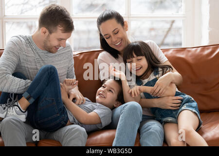 Glückliche Eltern mit Kindern kitzeln lachend spielen auf einem Sofa zusammen Stockfoto