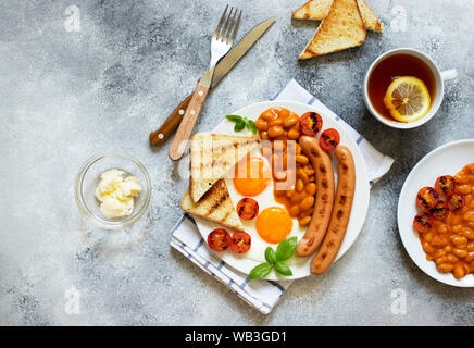 Englisches Frühstück mit gebratenen Würstchen, Bohnen, Pilze, Spiegelei, gegrillten Tomaten. Grauer Hintergrund Stockfoto