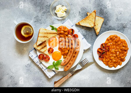 Englisches Frühstück mit gebratenen Würstchen, Bohnen, Pilze, Spiegelei, gegrillten Tomaten. Grauer Hintergrund Stockfoto