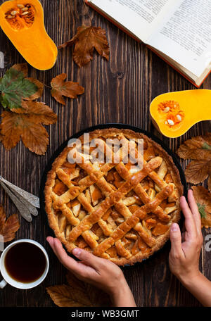 Weibliche Hände halten hausgemachte Kürbiskuchen. Halloween und Thanksgiving. Urlaub Kürbis Süßigkeiten. Holz Herbst Hintergrund, trockene Blätter, schneiden Kürbis, Kaffee Stockfoto