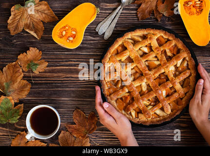 Weibliche Hände halten hausgemachte Kürbiskuchen. Halloween und Thanksgiving. Urlaub Kürbis Süßigkeiten. Holz Herbst Hintergrund, trockene Blätter, schneiden Kürbis, Kaffee Stockfoto