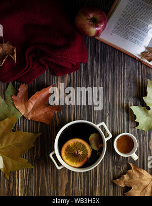 Warme Herbst und Winter alkoholisches Getränk Glühwein. Honig, Herbstblätter, Äpfel, ein Buch und einen wollpullover auf einer hölzernen Hintergrund. Herbst gemütliche Stimmung Stockfoto