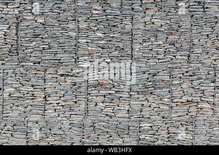 Eine Wand mit kleinen grauen Steine hinter einem Gitter aus Metall ausgekleidet, so dass die Berge bröckeln nicht. Stein Textur Stockfoto