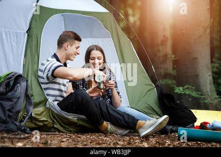 Romantisches Paar Camping im Freien und trinken Tee aus der Thermoskanne, während in der Nähe des Zeltes sitzen Stockfoto