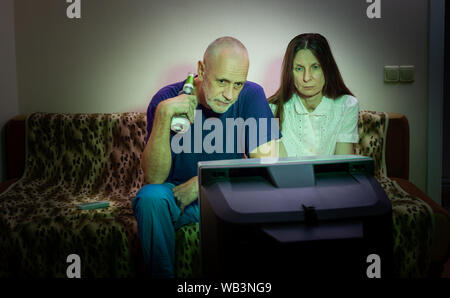Im mittleren Alter Mann und Frau, Fernsehen, traurig, sitzt auf einer Couch. Sie sehen einen traurigen Film oder zu den schlechten Nachrichten, die Sie ein wenig un Macht hören Stockfoto