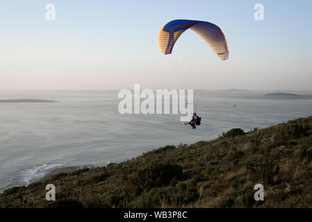 Ein Tandem Gleitschirm startet vom Signal Hill oberhalb der Stadt Kapstadt am Atlantik Südafrika's Küste mit Robben Island am Horizont Stockfoto