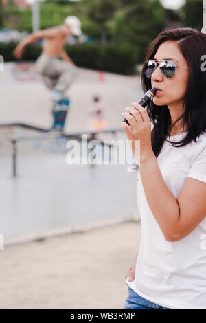 Junge Frau rauchen mit der elektronischen Zigarette auf einem Skateboard Park Stockfoto