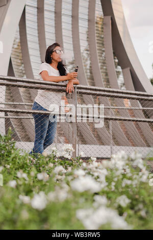 Junge Frau mit Sonnenbrille auf einem malerischen Brücke mit einem elektronischen Zigarette rauchen Stockfoto