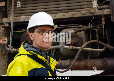 Männliche Arbeiter in einen Helm vor dem Hintergrund der hydraulischen Antriebe von Baumaschinen Stockfoto