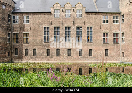 Helmond, Niederlande, 16. August 2019: Blick über den Burggraben und Schilf und Wildblumen auf seiner Bank gegenüber der sonnendurchfluteten Südfassade des 14 Cent Stockfoto