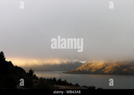 Sunrise durch den Nebel vor einem Berg und dem See in der Nähe von Queenstown in Neuseeland Stockfoto