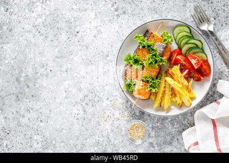 Gegrillter Lachs Kebab am Spieß mit gebackenen Kartoffeln, frischen Gurken und Tomaten Stockfoto