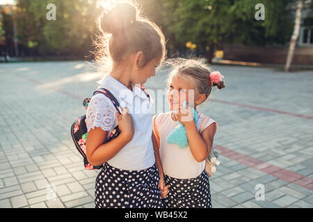 Glückliche Schwestern Mädchen, Rucksäcke und halten sich an den Händen. Kinder, Schüler gehen nach dem Unterricht im Freien Grundschule. Bildung. Zurück zur Schule Stockfoto