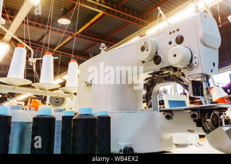 Fragment des Inneren eines Nähwerkstatt mit verschiedenen Geräten, Hülsen der Gewinde- und industriellen Nähmaschine im Vordergrund. Stockfoto