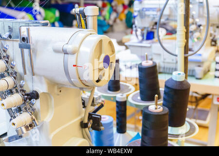 Fragment des Inneren eines Nähwerkstatt mit verschiedenen Geräten, Hülsen der Gewinde- und industriellen Nähmaschine im Vordergrund. Stockfoto