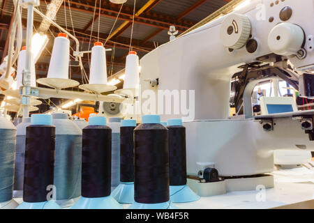 Fragment des Inneren eines Nähwerkstatt mit verschiedenen Geräten, Hülsen der Gewinde- und industriellen Nähmaschine im Vordergrund. Stockfoto