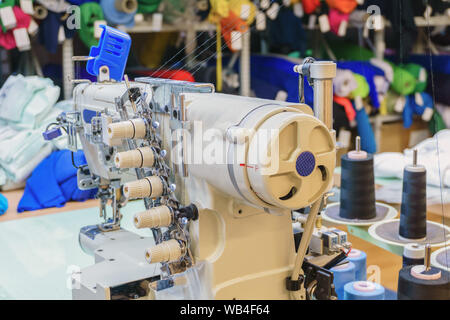 Fragment des Inneren eines Nähwerkstatt mit verschiedenen Geräten, Hülsen der Gewinde- und industriellen Nähmaschine im Vordergrund. Stockfoto