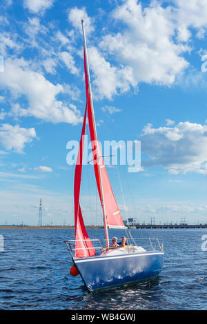 Zwei Männer sind segeln auf einer kleinen Yacht mit Scarlet Sails auf den Behälter vor dem Hintergrund der Dam Stockfoto