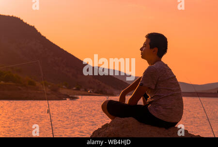 Emirdag/Afyonkarahisar - 11. August 2019: Angeln auf dem Boden und junge Fischer sitzen auf dem Rock implantiert und warten, um Fische zu fangen Stockfoto