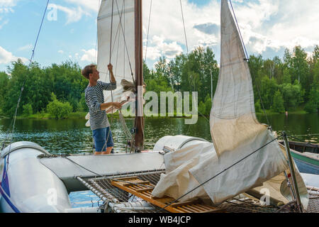 Junge sailor wirft ein Segel auf einer kleinen Segelyacht in einem bewaldeten Bucht günstig Stockfoto