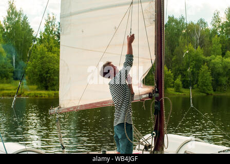 Junge sailor wirft ein Segel auf einer kleinen Segelyacht in einem bewaldeten Bucht günstig Stockfoto