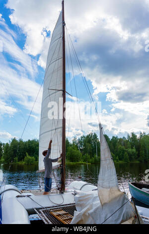 Junge sailor wirft ein Segel auf einer kleinen Segelyacht in einem bewaldeten Bucht günstig Stockfoto