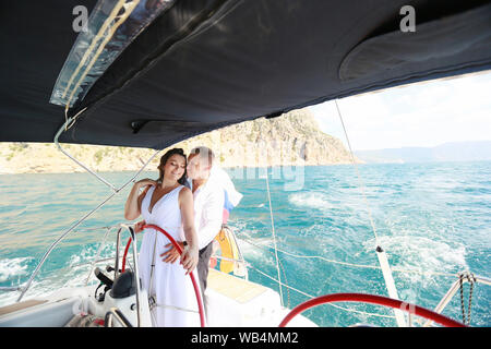 Weiße Yacht mit Segel setzen geht entlang der Insel an einem heißen Tag. blaues Meer, blauer Himmel. Krim. an Bord ein junges Paar in der Liebe. die Braut und der Bräutigam. weddin Stockfoto