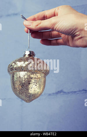 Glas acorn Weihnachten Dekoration in der Hand gegen die helle Farbe Wand. Urlaub Christbaumschmuck Stockfoto