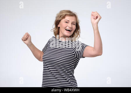 Schöne, reife Frau in Freizeitkleidung mit einem herzlichen Lächeln posing Tanzen mit Händen auf rosa Hintergrund. Positive facial menschliches Gefühl. Studio shot Stockfoto